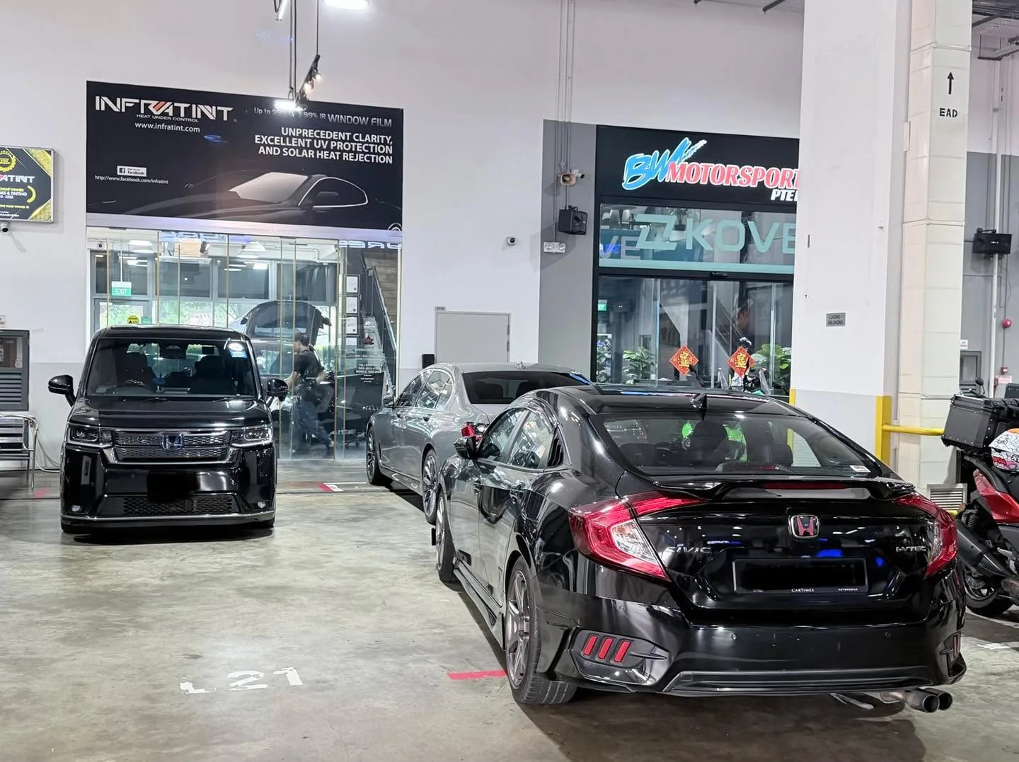 A black Honda Civic sedan at an angle in the workshop, with a silver vehicle visible behind it.