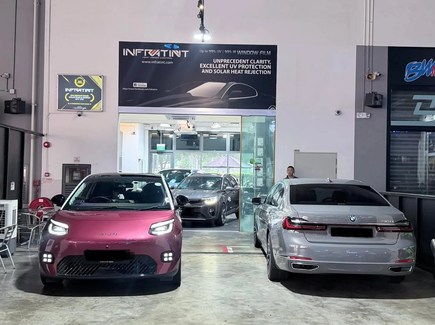 A maroon Aion hatchback with white and silver cars in the workshop background.
