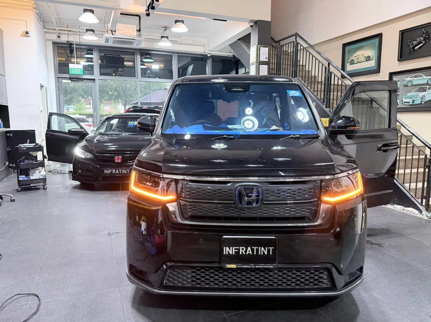 A red Honda CR-V with amber headlights and a black sedan to the left in the workshop.