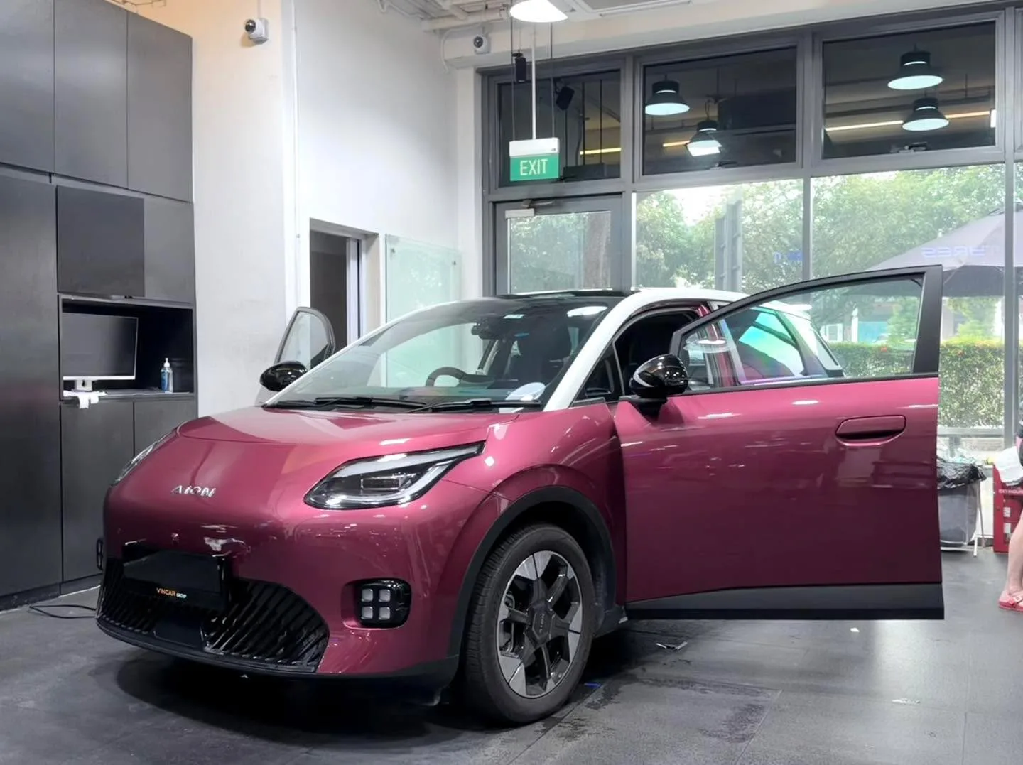 A dark blue electric hatchback with the driver's window being worked on by a technician.