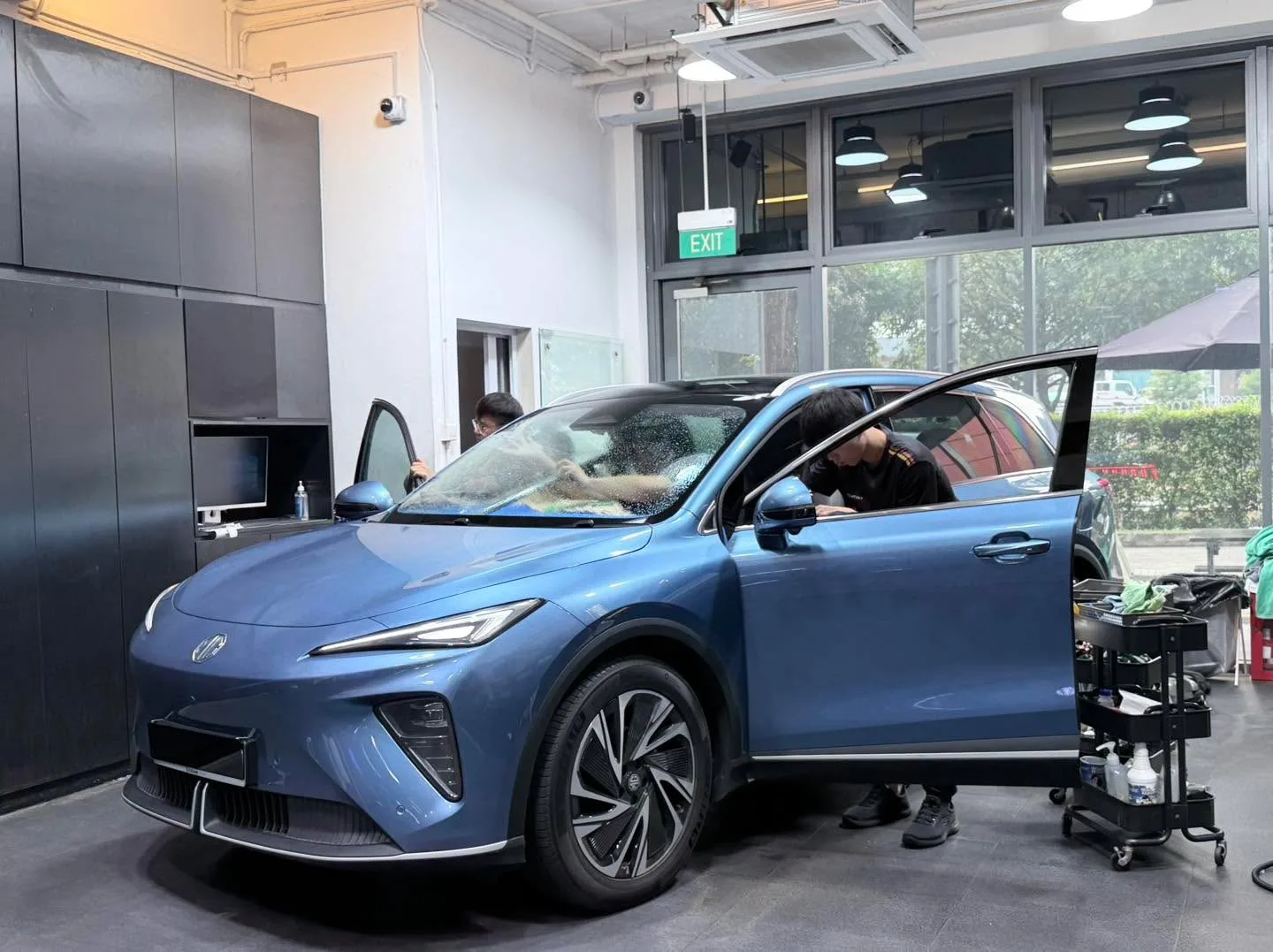 A light blue electric crossover viewed from the side with a technician working on the window.