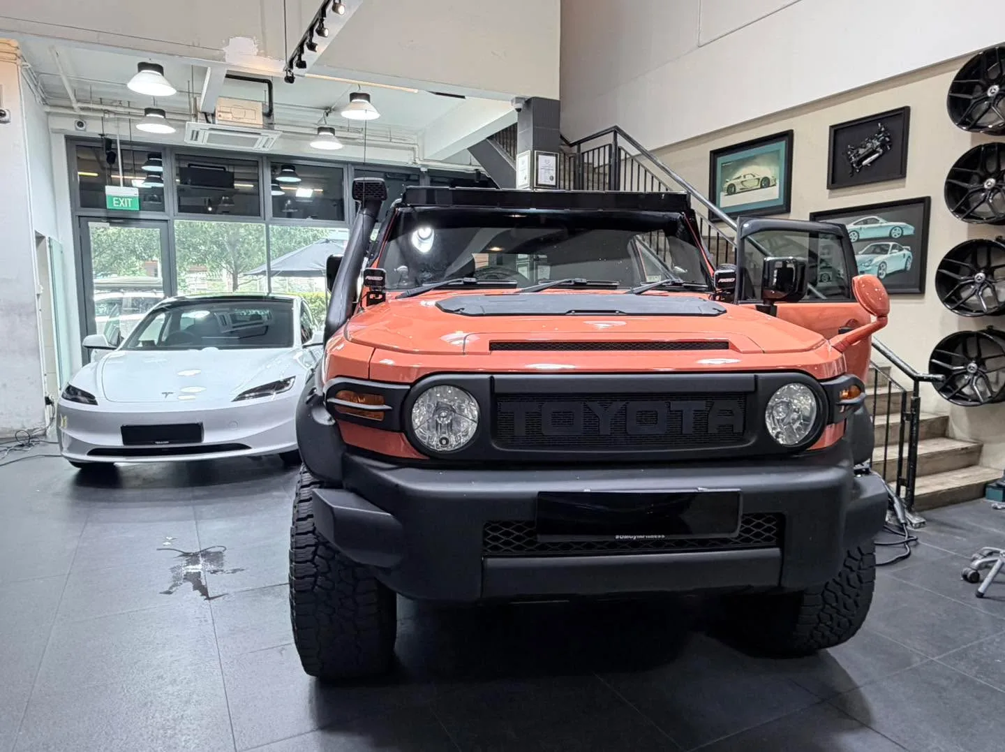 An orange Toyota FJ Cruiser with doors open facing forward in a workshop.