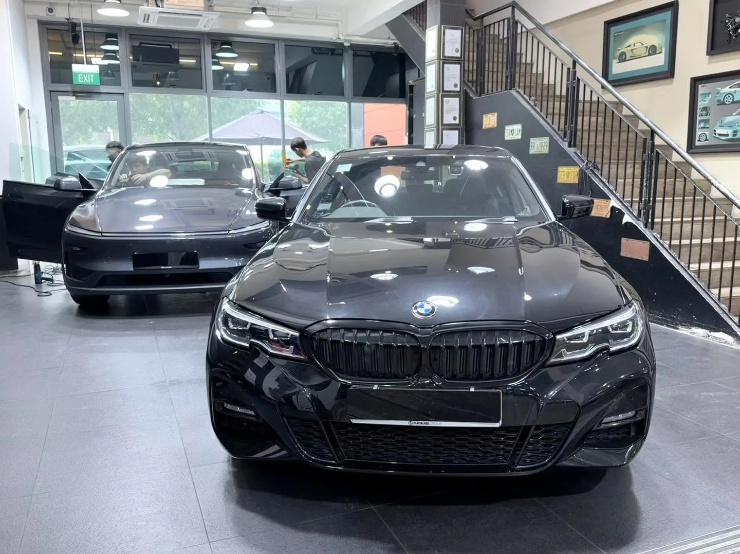 A black BMW saloon and a black Tesla parked side by side in a workshop.