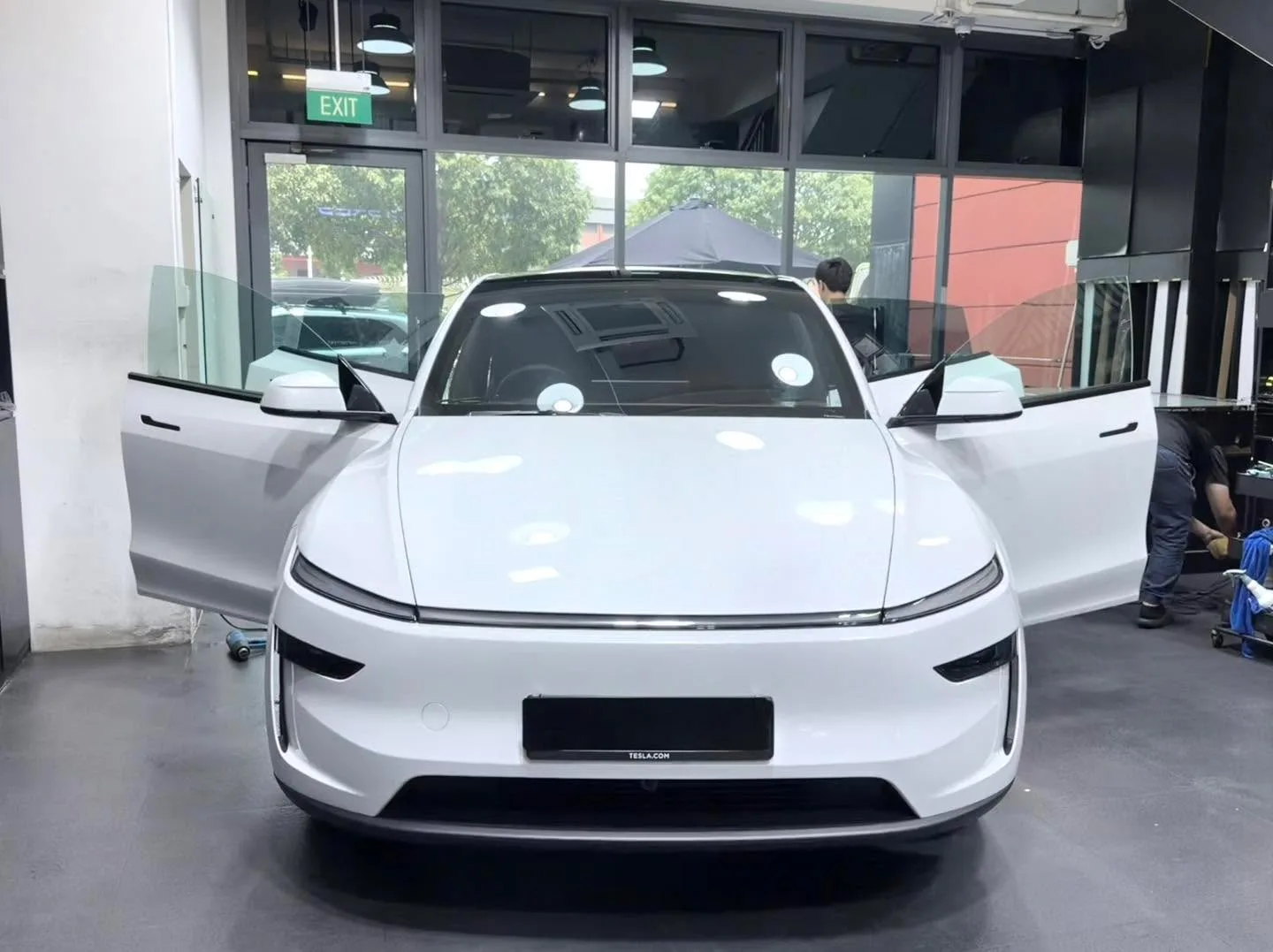 A white Tesla saloon with doors open in a workshop, facing forward.