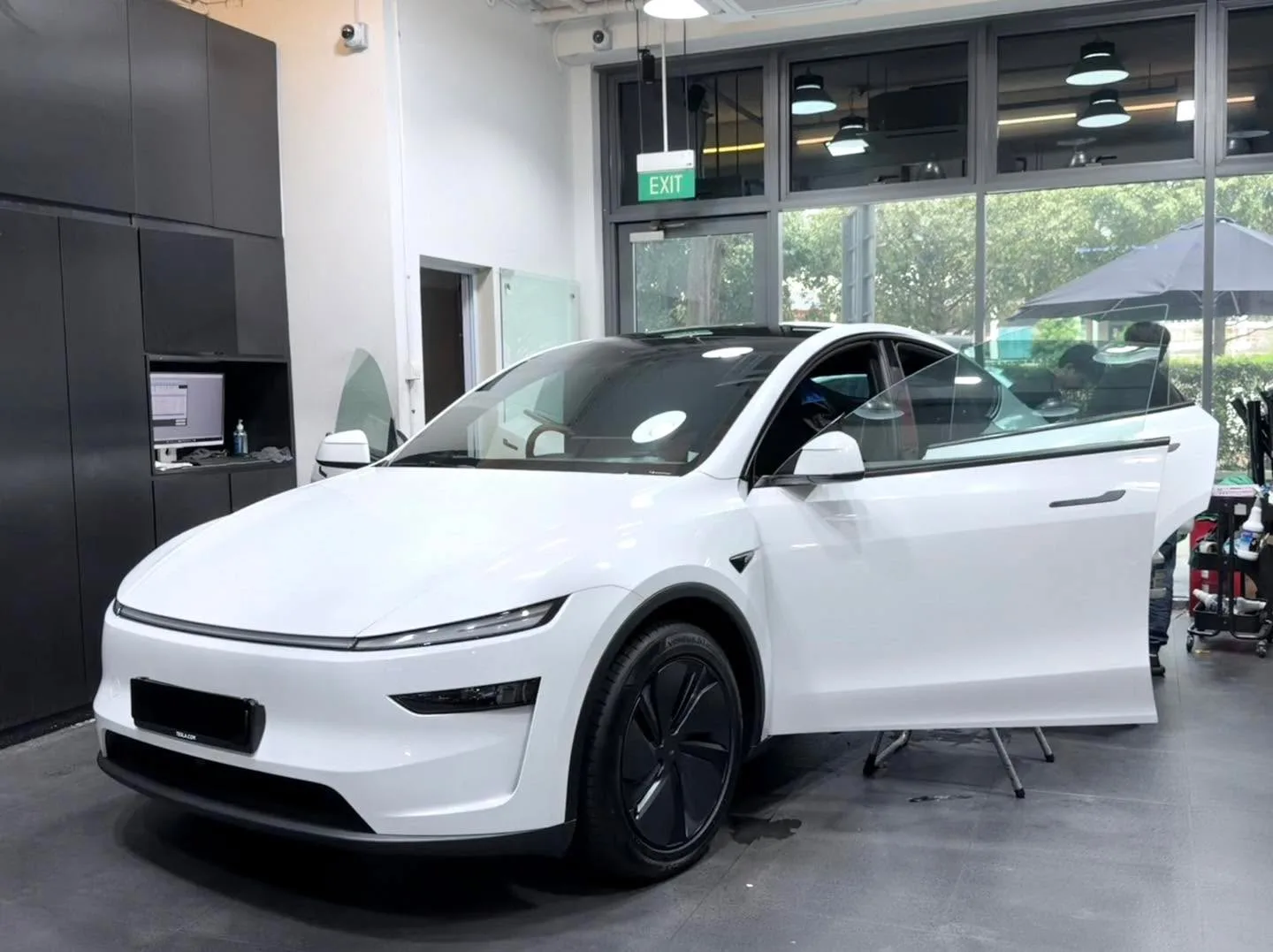 A white Tesla saloon with doors open in a workshop space.