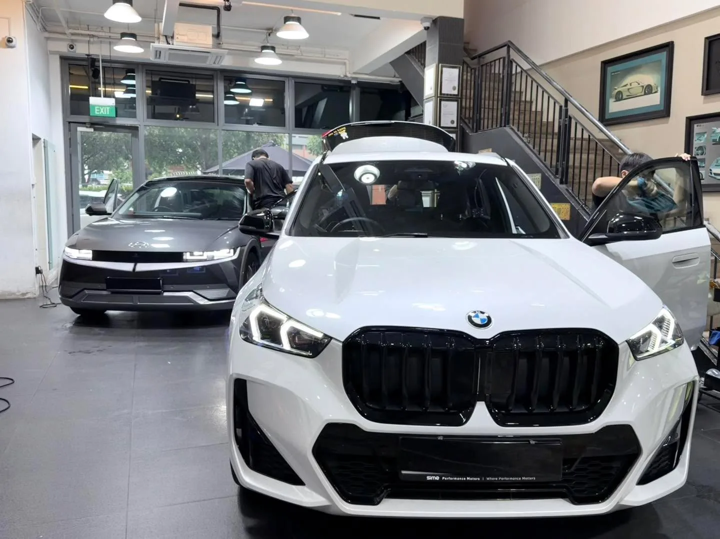 A white BMW X1 SUV with its door open, positioned in the workshop bay.