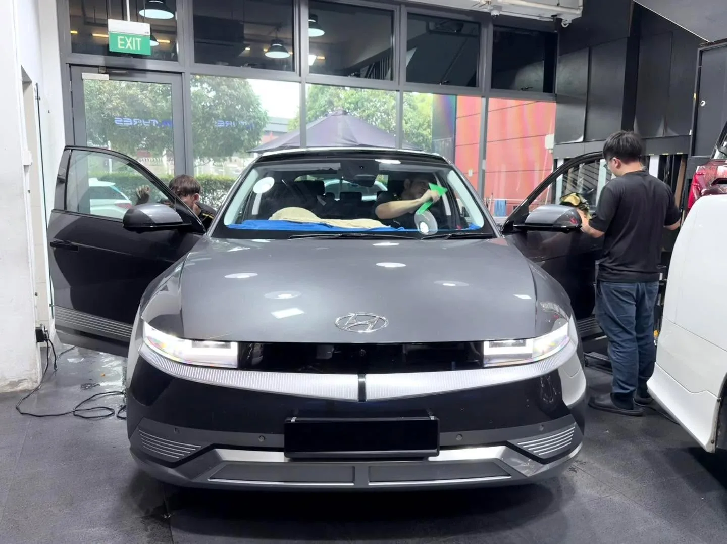 A grey Hyundai Ioniq sedan with doors open, being worked on by technicians.