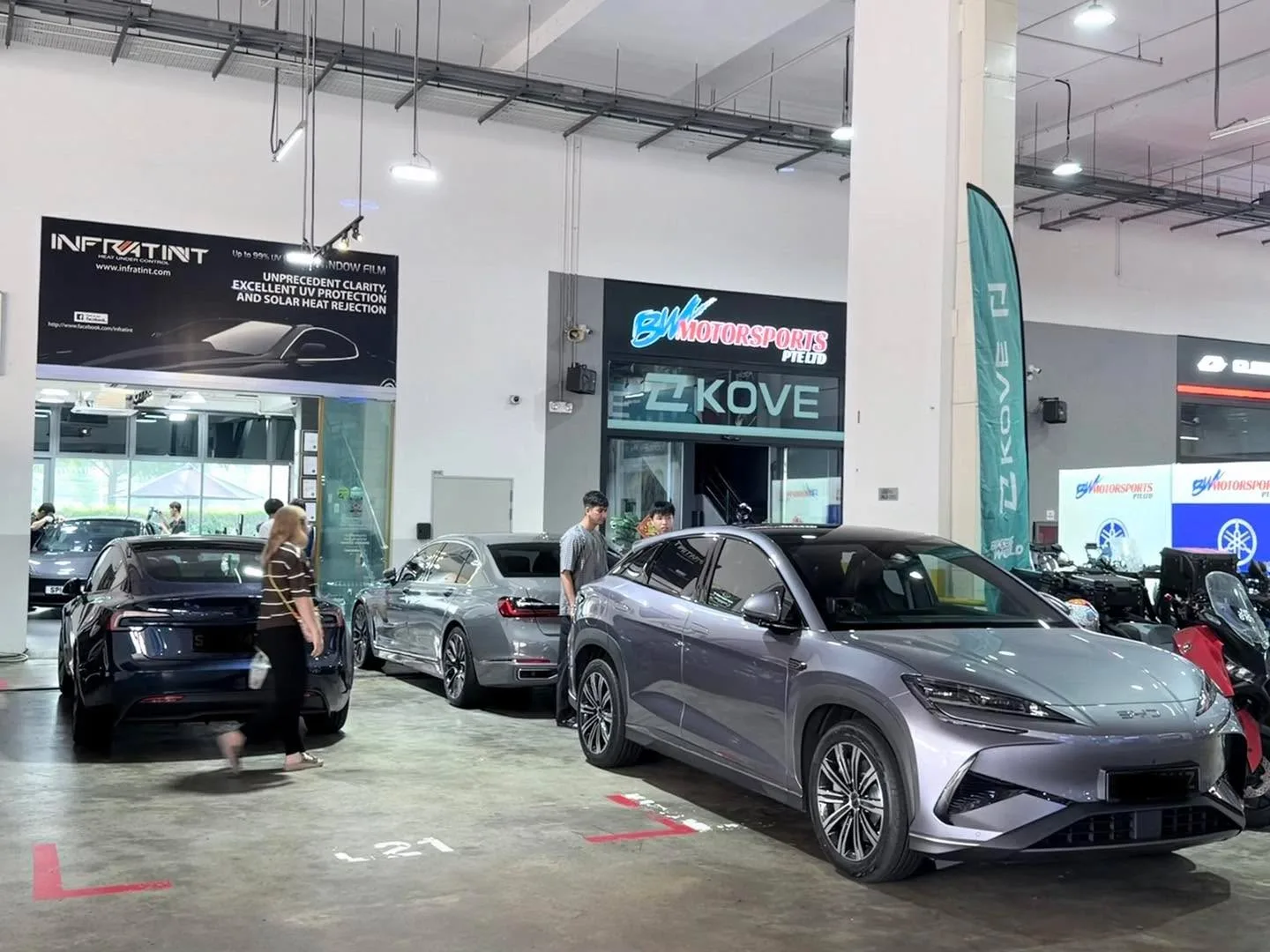 A dark blue saloon, a silver sedan, a white multi-purpose vehicle and a silver sedan parked in an indoor workshop.