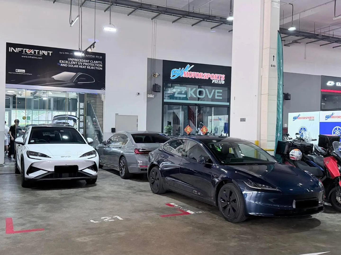 A white saloon, a silver sedan, a dark blue sedan and a white multi-purpose vehicle in the workshop.