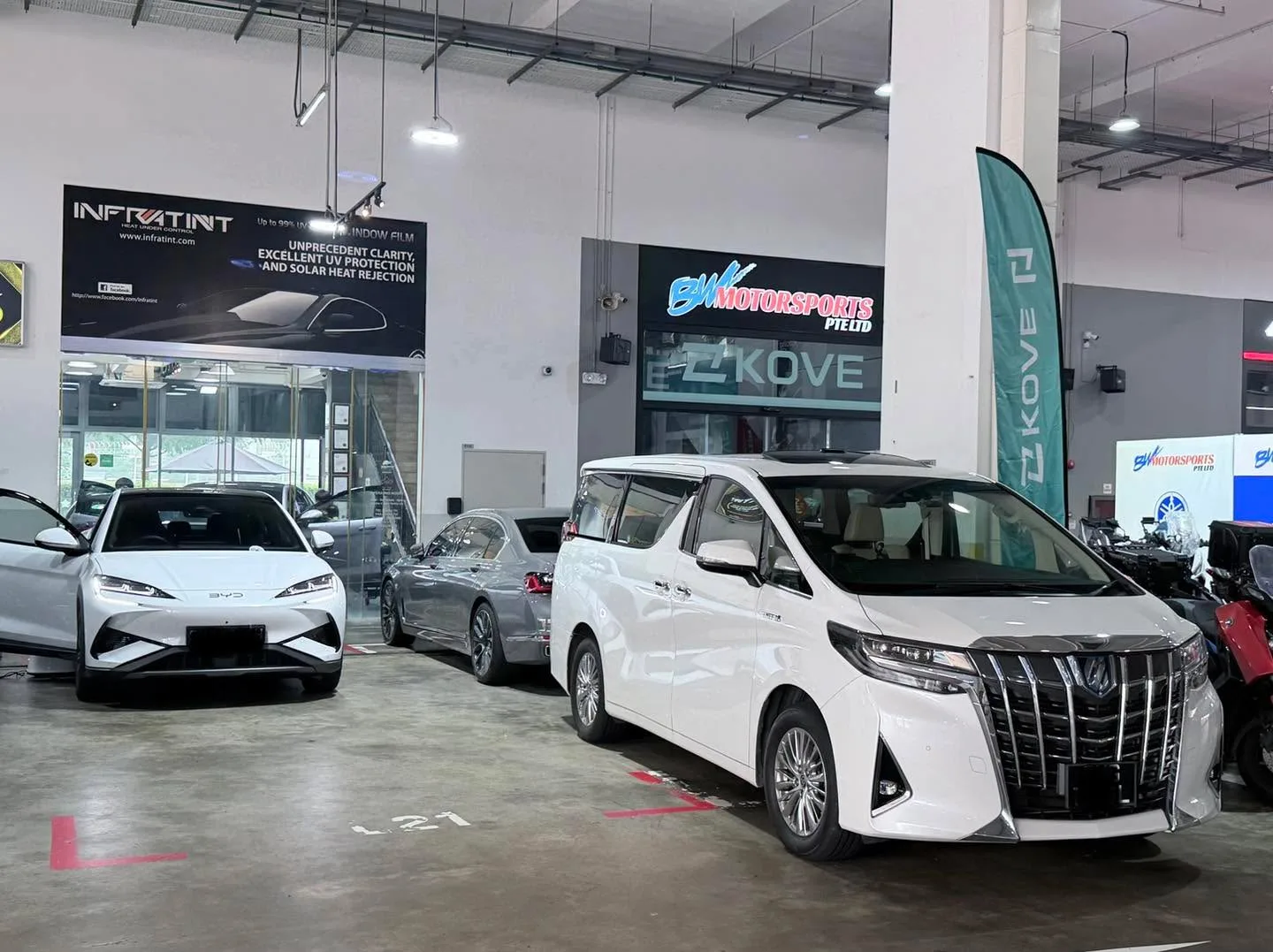 A white saloon, a silver sedan and a white multi-purpose vehicle with distinctive grille in the workshop.