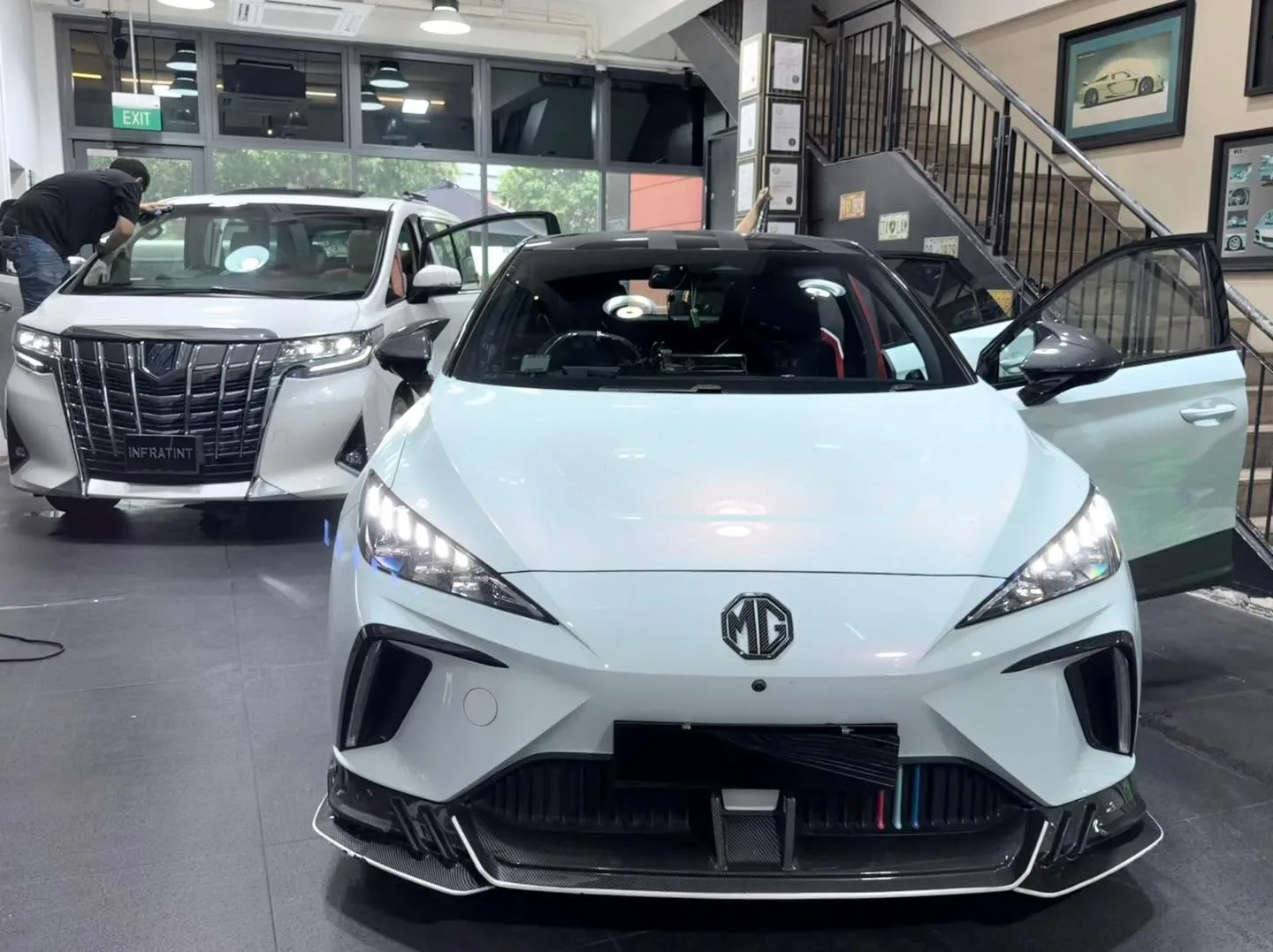A white MG 4 hatchback and a white BYD sedan in the workshop interior.