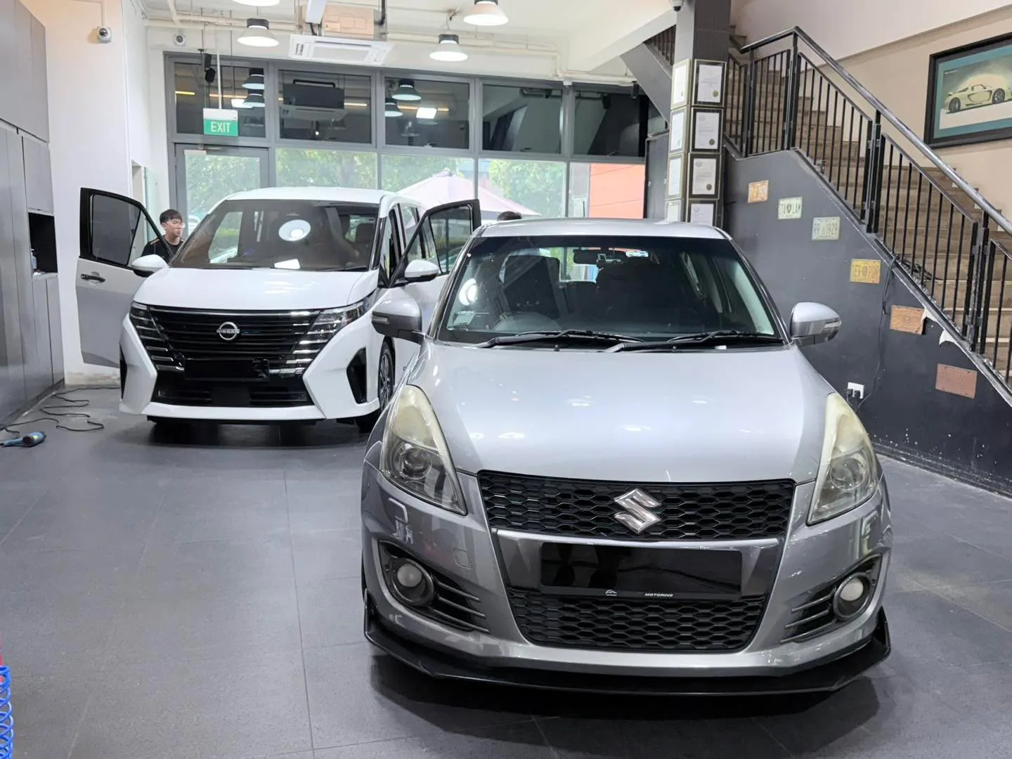A silver Suzuki Swift and white Nissan Serena stand in the workshop bay.