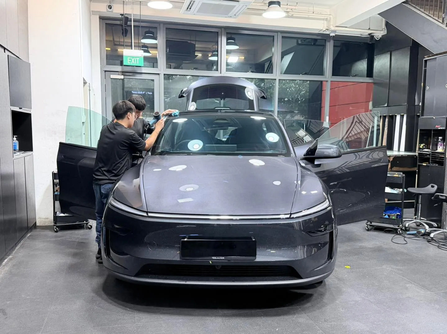A dark grey Tesla Model Y has its front windscreen tinted by a technician.