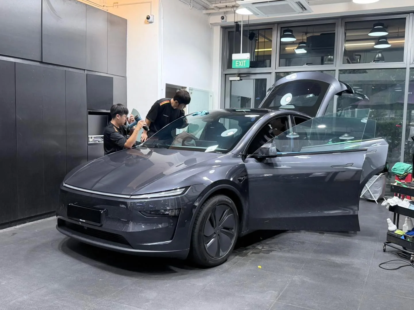 Two technicians apply window tint to a dark grey Tesla hatchback.