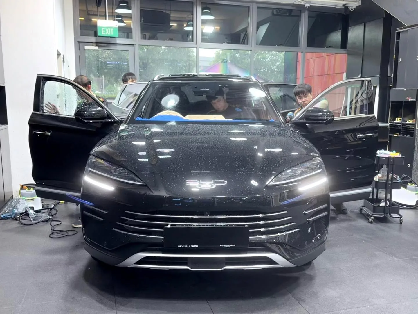 A black compact SUV with doors open, viewed from the front, with staff working inside the workshop.