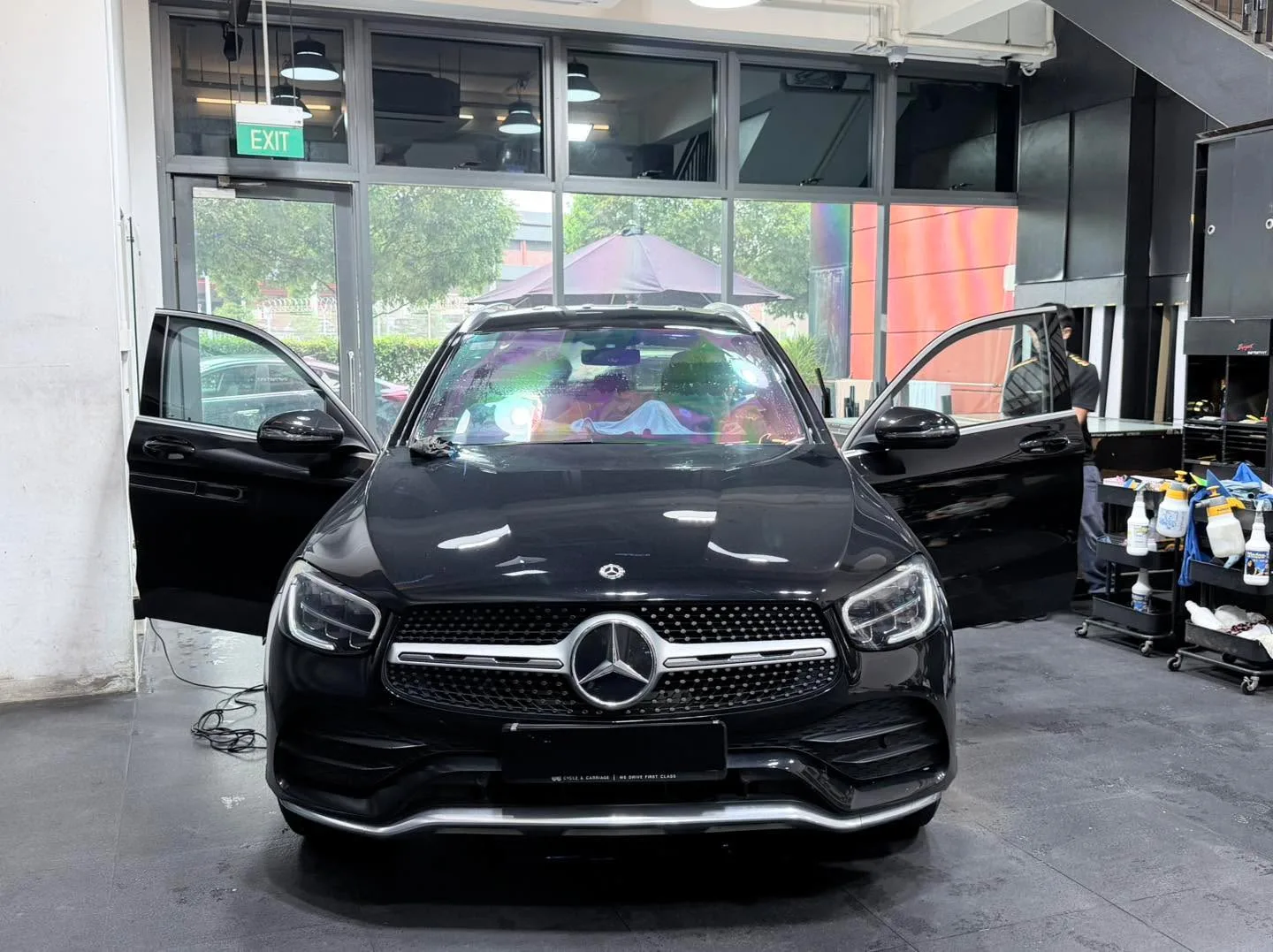 A black compact SUV with doors open, viewed head-on in the workshop with staff present.
