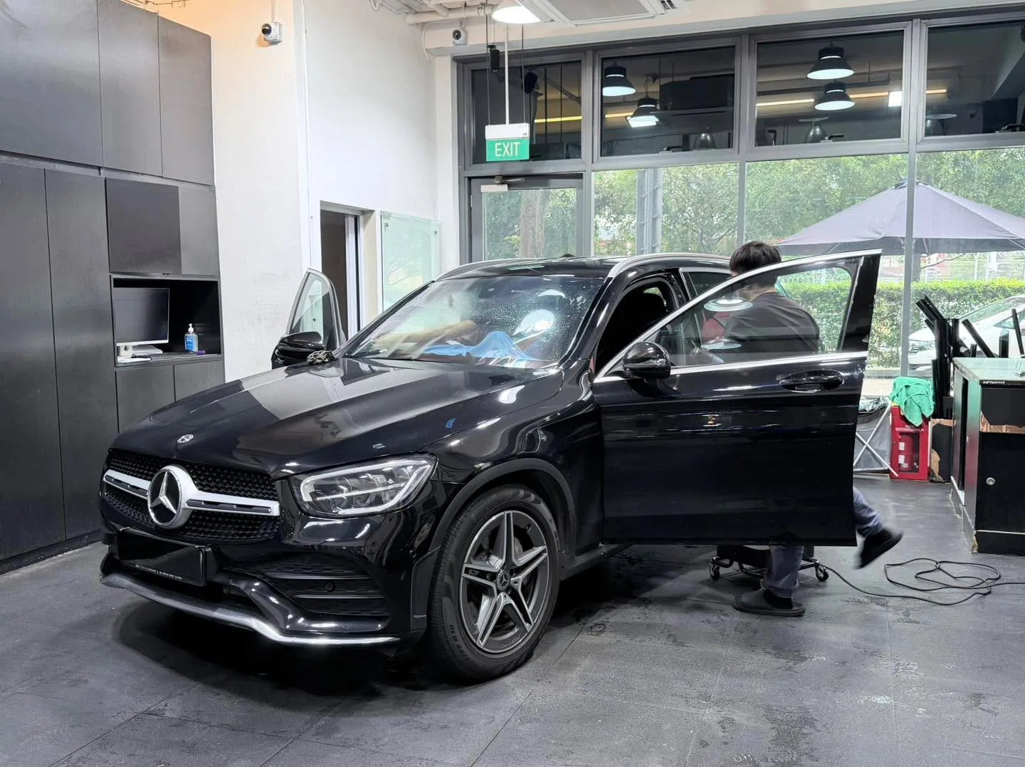 A black compact SUV photographed from the side with door open, staff applying window tint.