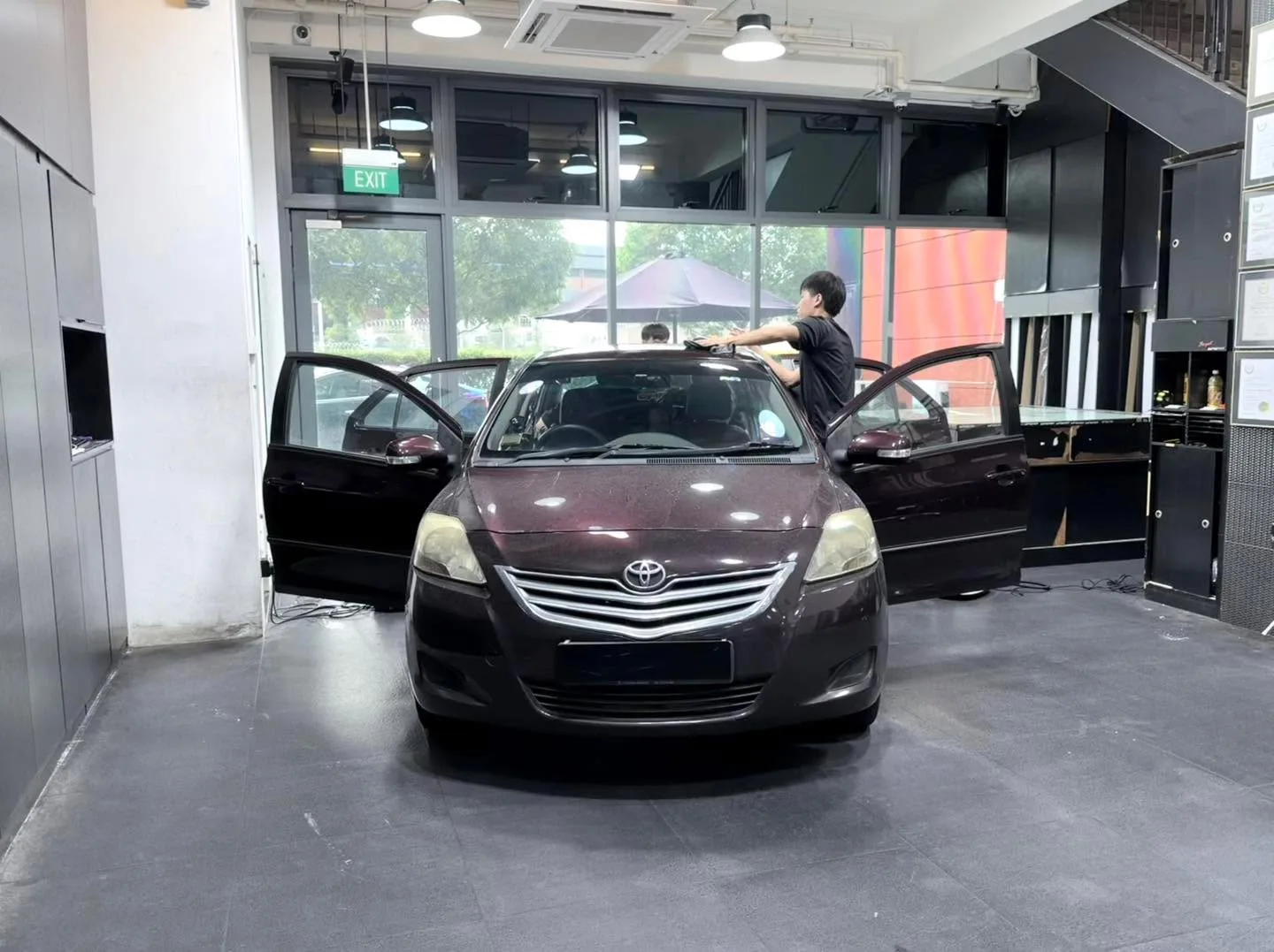 A dark maroon compact sedan with doors open, interior visible, staff tinting windows above.