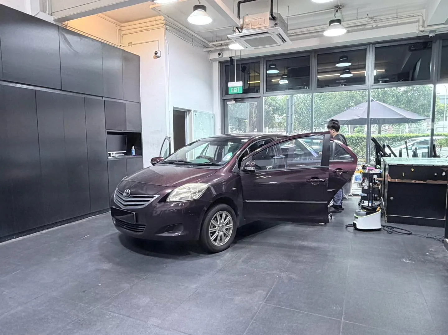 A dark maroon compact sedan photographed from the side with door open, staff applying film.