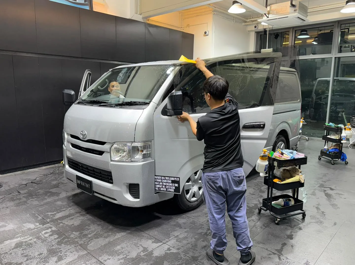 A white van with large windows, staff applying tint film to the side glass.