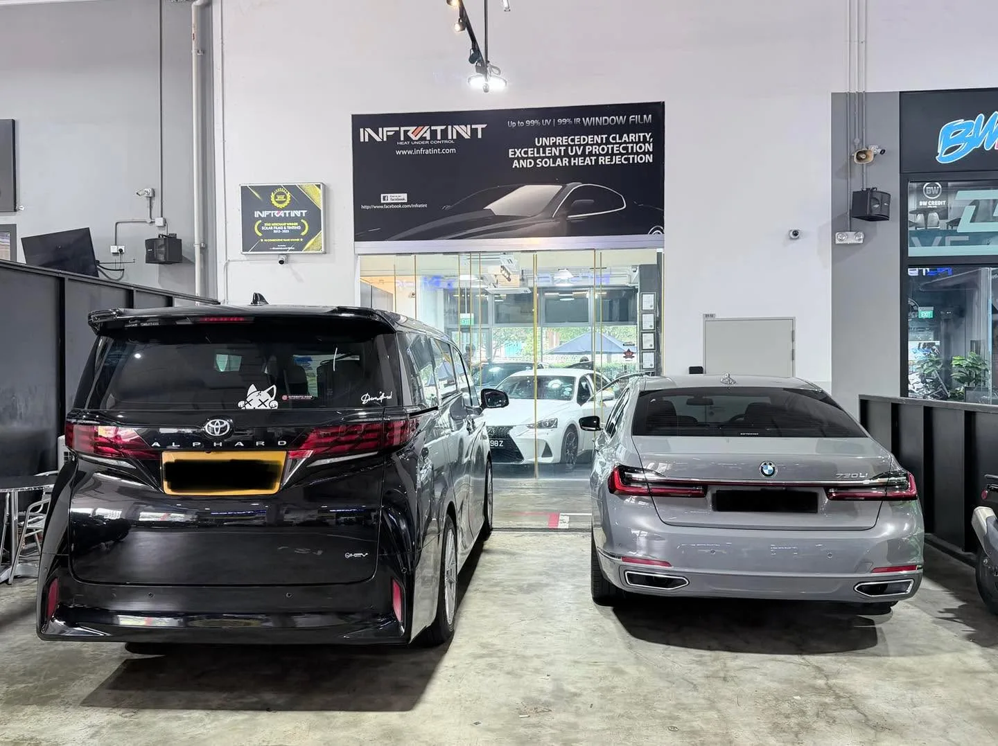 A black multi-purpose vehicle with red tail lights and a grey sedan in the workshop.
