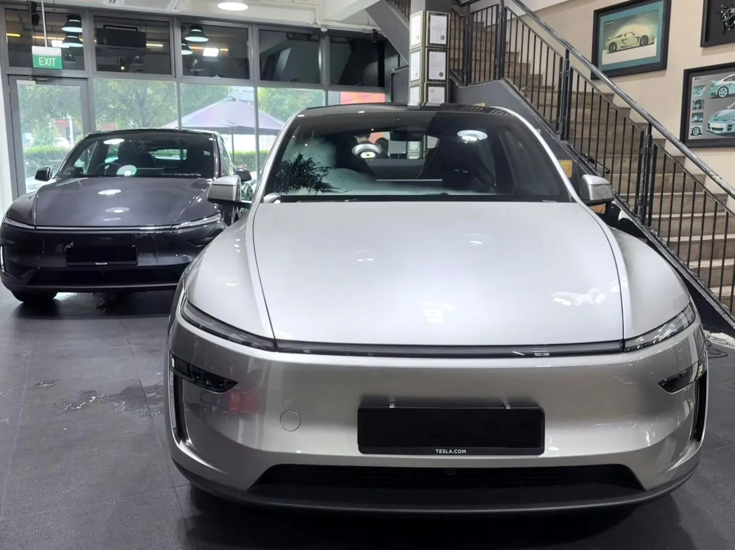 Two cars parked indoors with a showroom backdrop. Left: black Hyundai Avante. Right: silver Tesla Model 3 Highland.