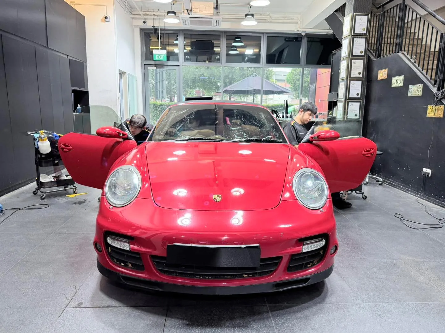 Bright red Porsche 911 Turbo with doors open undergoing window film treatment. Two technicians work on the sports car.