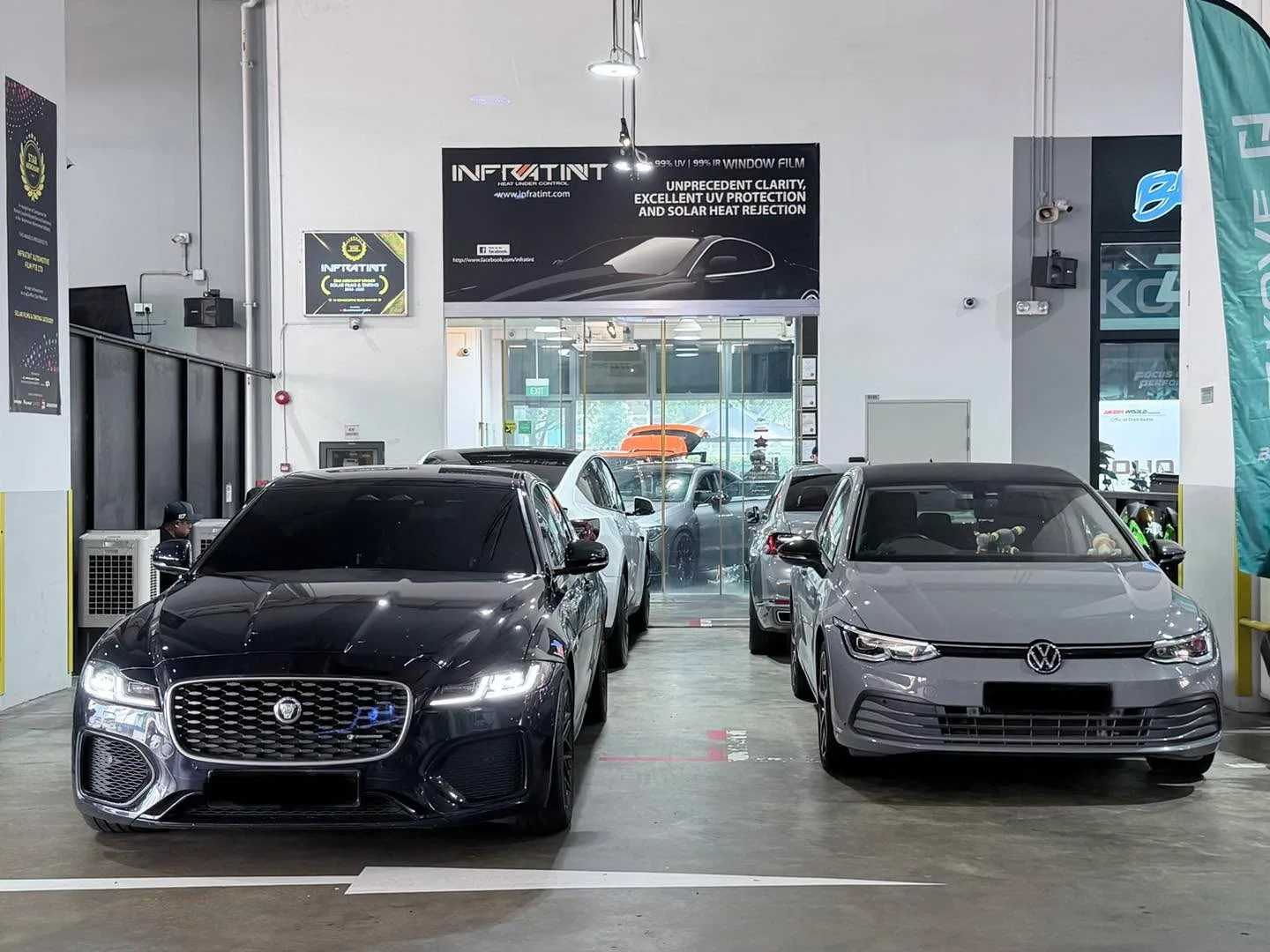 A black Jaguar XF sedan and a silver Volkswagen Golf hatchback parked side by side in the workshop.