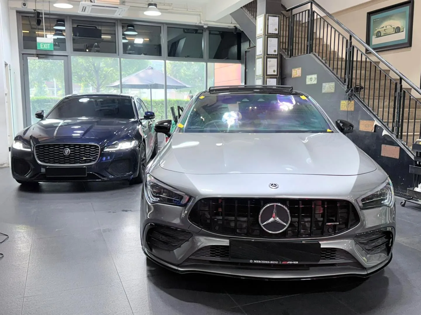 A silver Mercedes-Benz CLA sedan and a black Jaguar XF sedan positioned in the workshop.