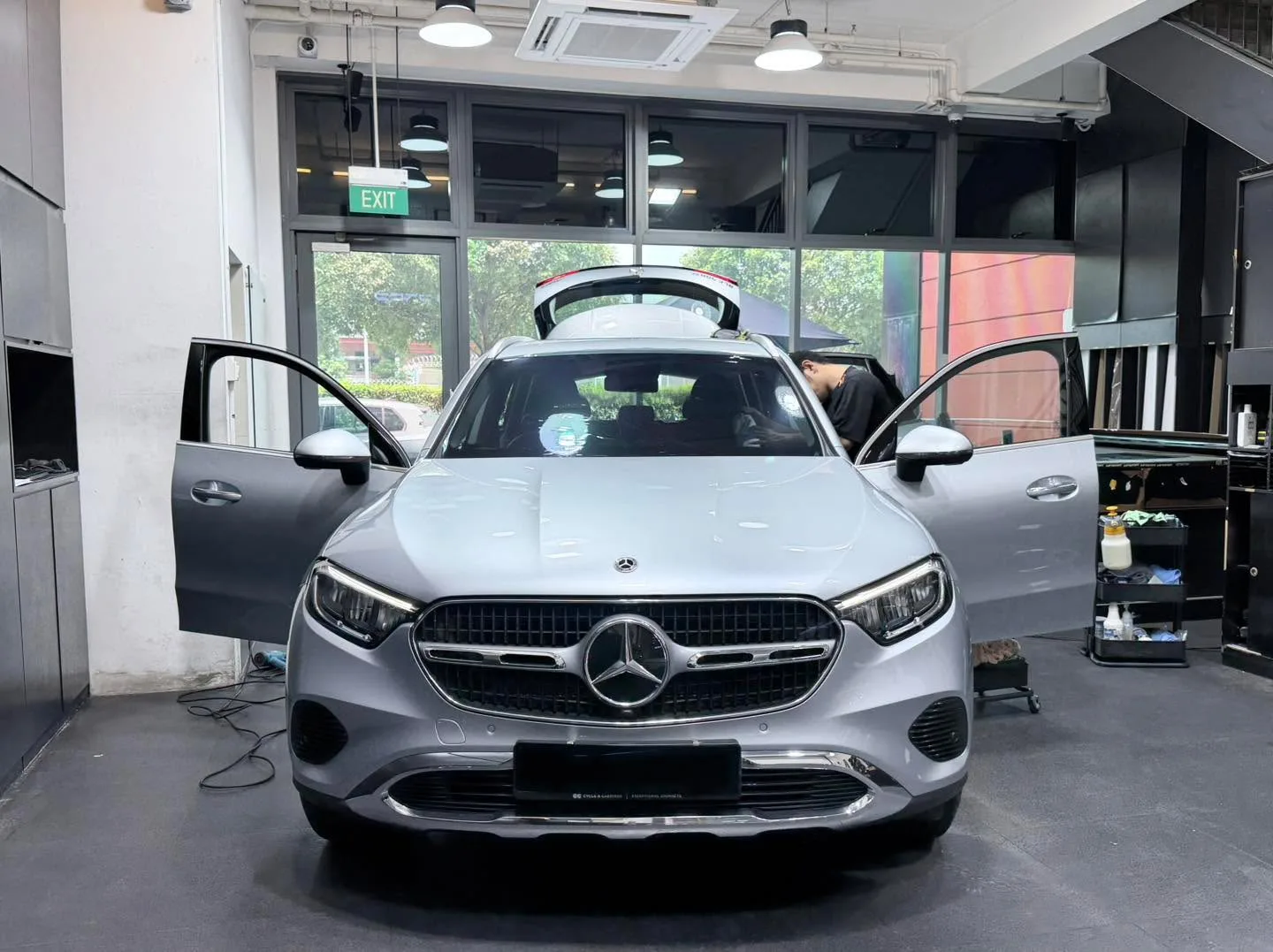 A silver Mercedes-Benz GLC SUV with both doors open, positioned front-facing in the workshop.