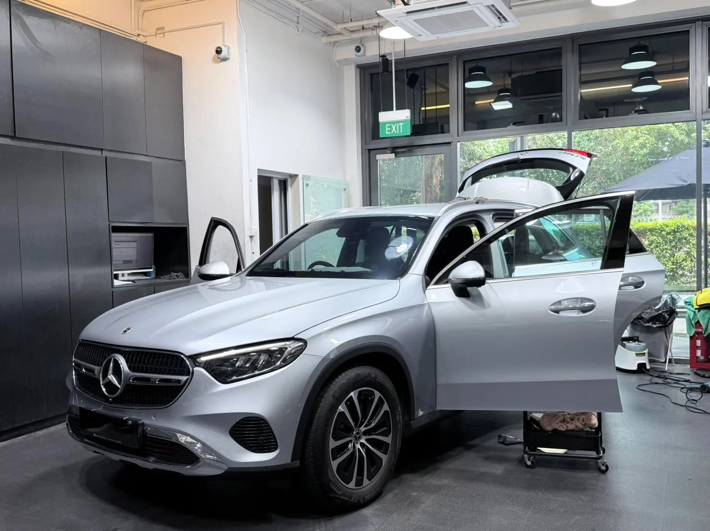 A silver Mercedes-Benz GLC SUV with both doors open, with staff applying window tint.