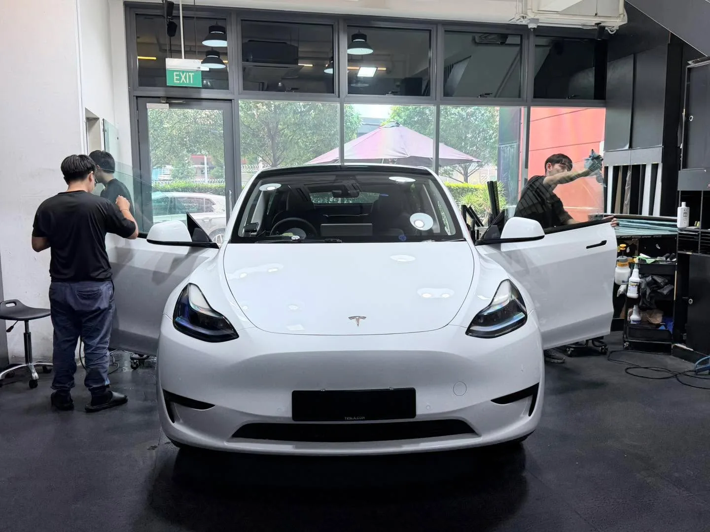 A white Tesla Model Y with doors open, with staff applying window film inside the workshop.