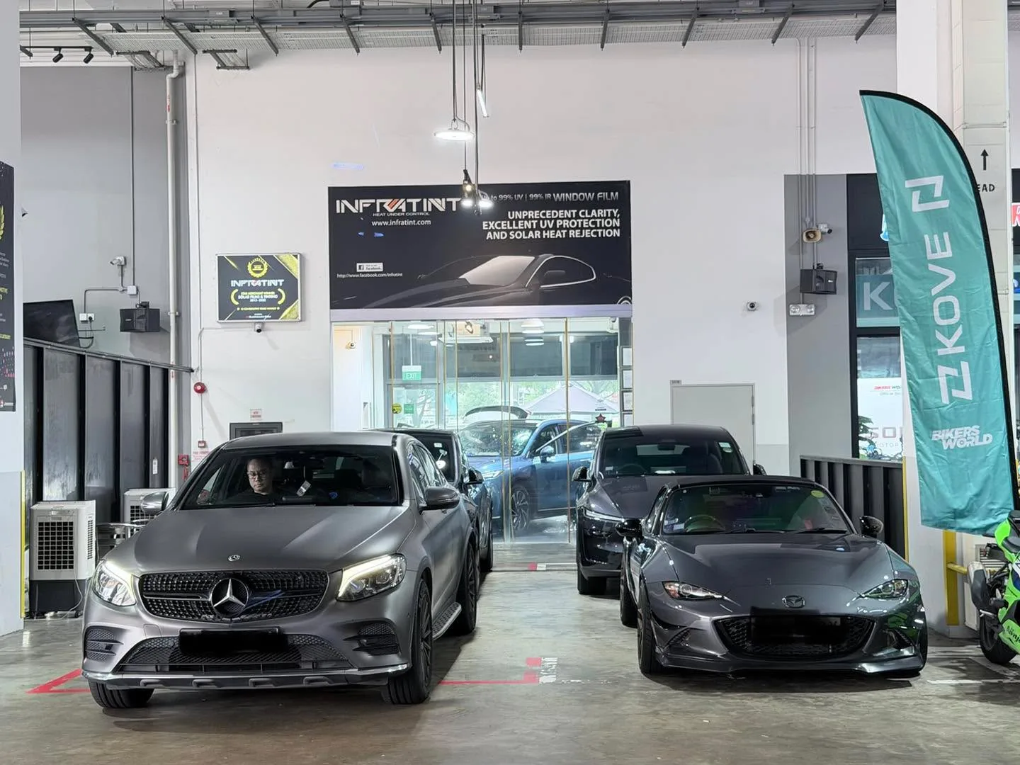 A silver Mercedes-Benz coupe and a dark grey sports car parked in the workshop.
