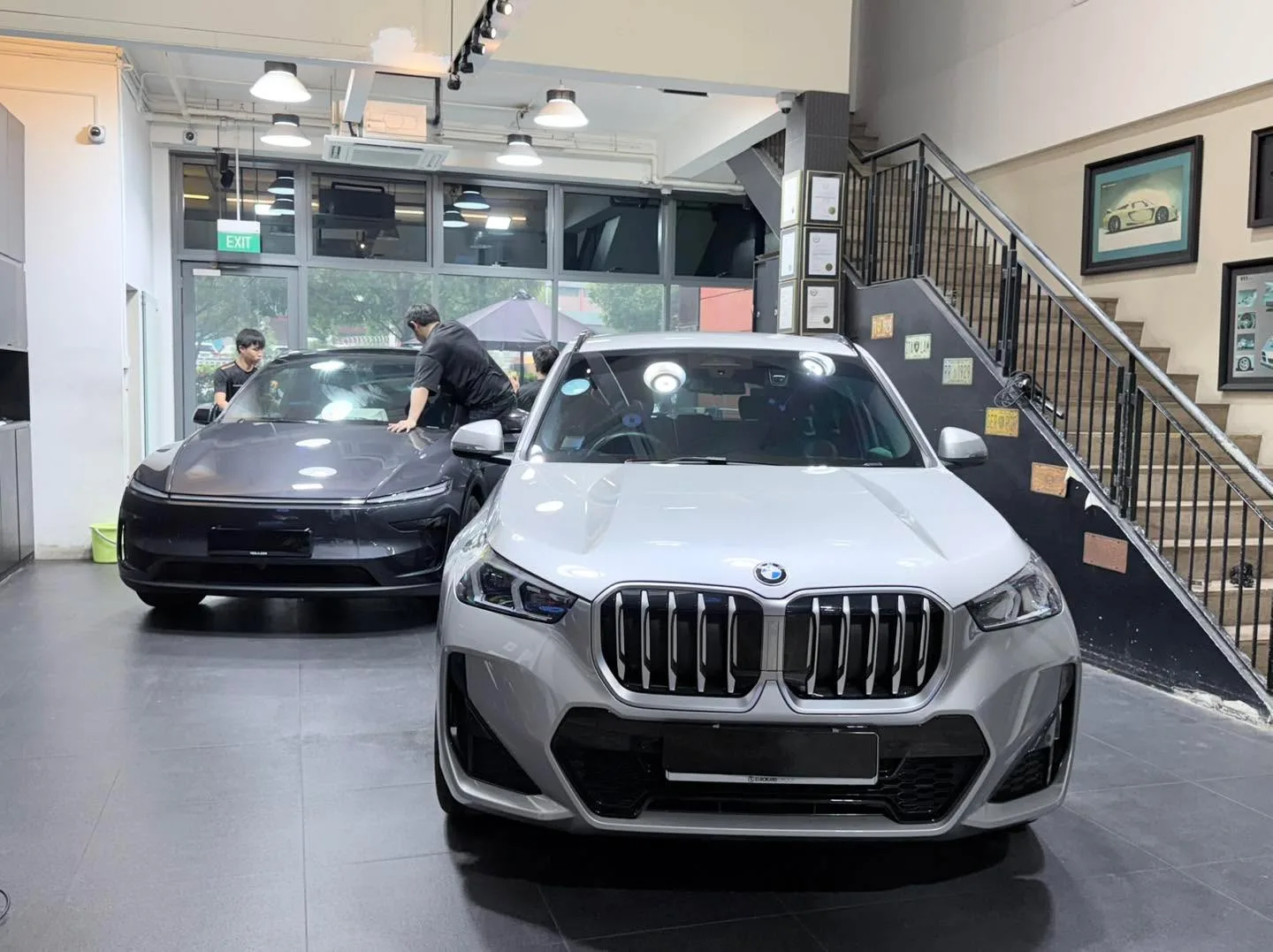 A silver BMW X1 SUV, front view, with a dark sedan in the background.