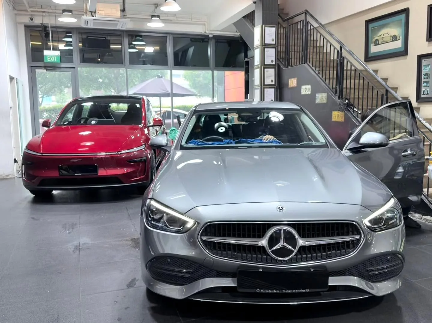 A red Tesla Model Y and a silver Mercedes-Benz sedan in the workshop.
