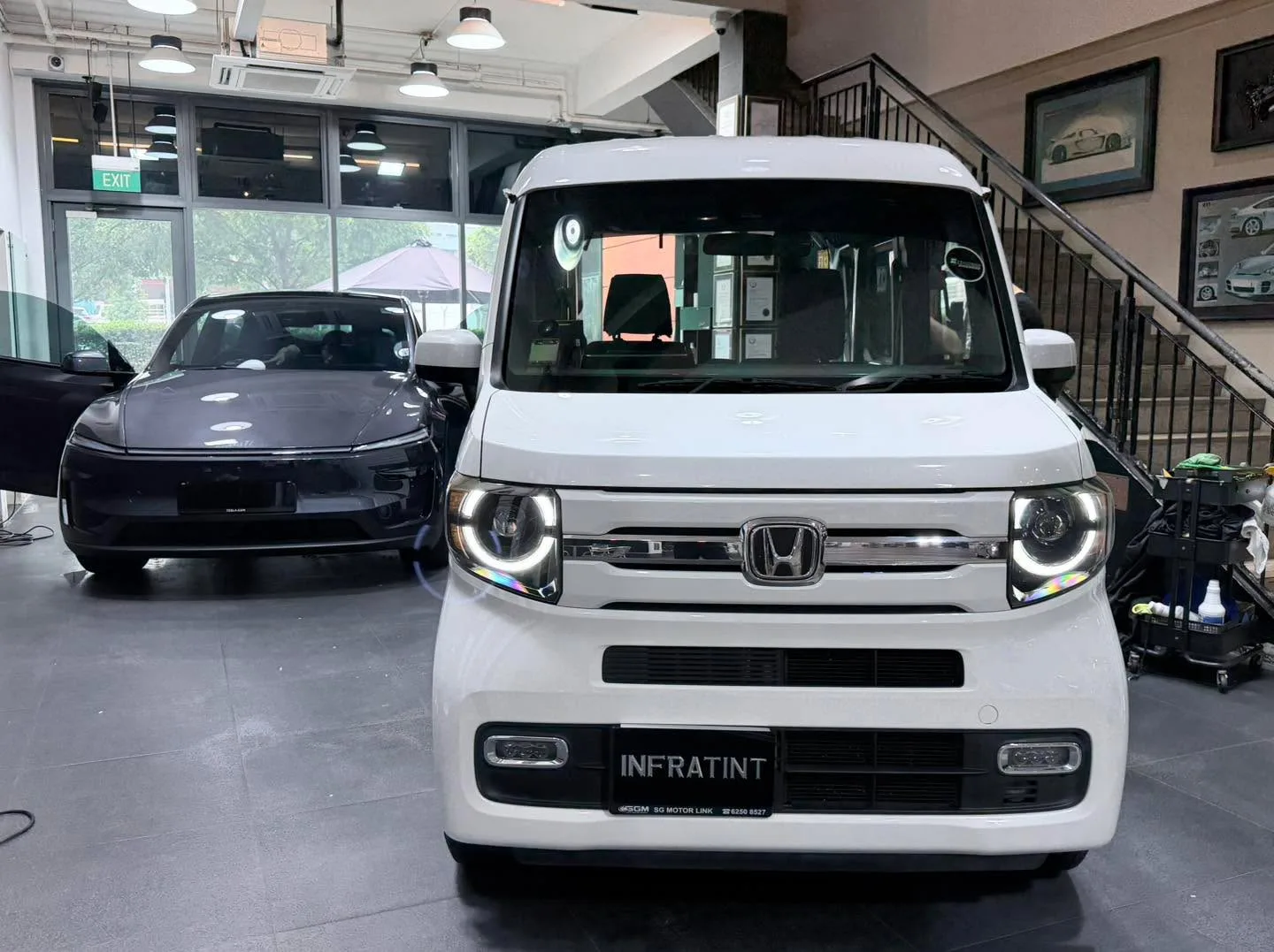 A white Honda compact vehicle, front view, with a dark sedan behind it.
