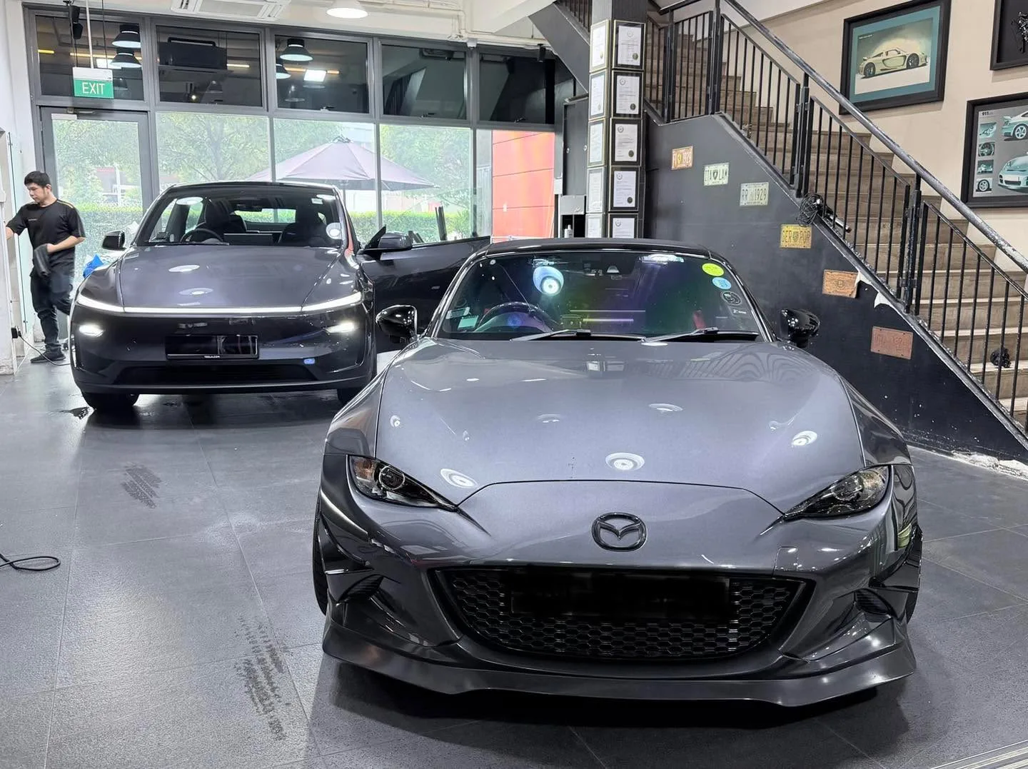 A dark Mazda sports car and a dark sedan with staff working inside the workshop.
