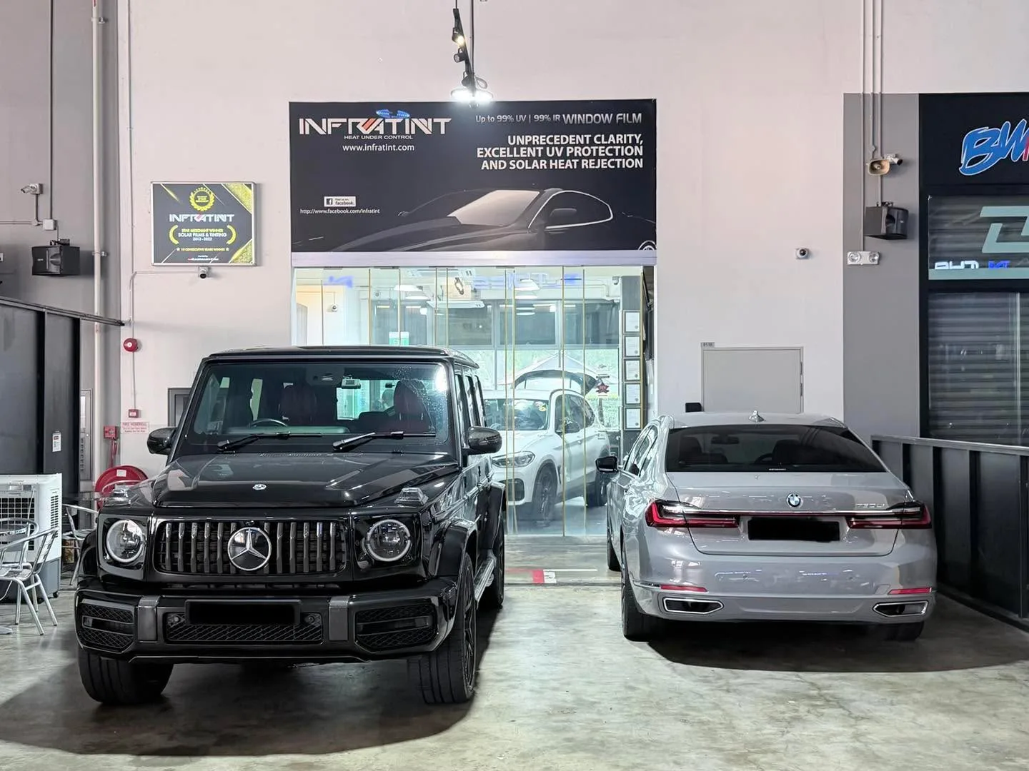 A black Mercedes-Benz G63 SUV and a silver BMW sedan parked in the workshop exterior bay.