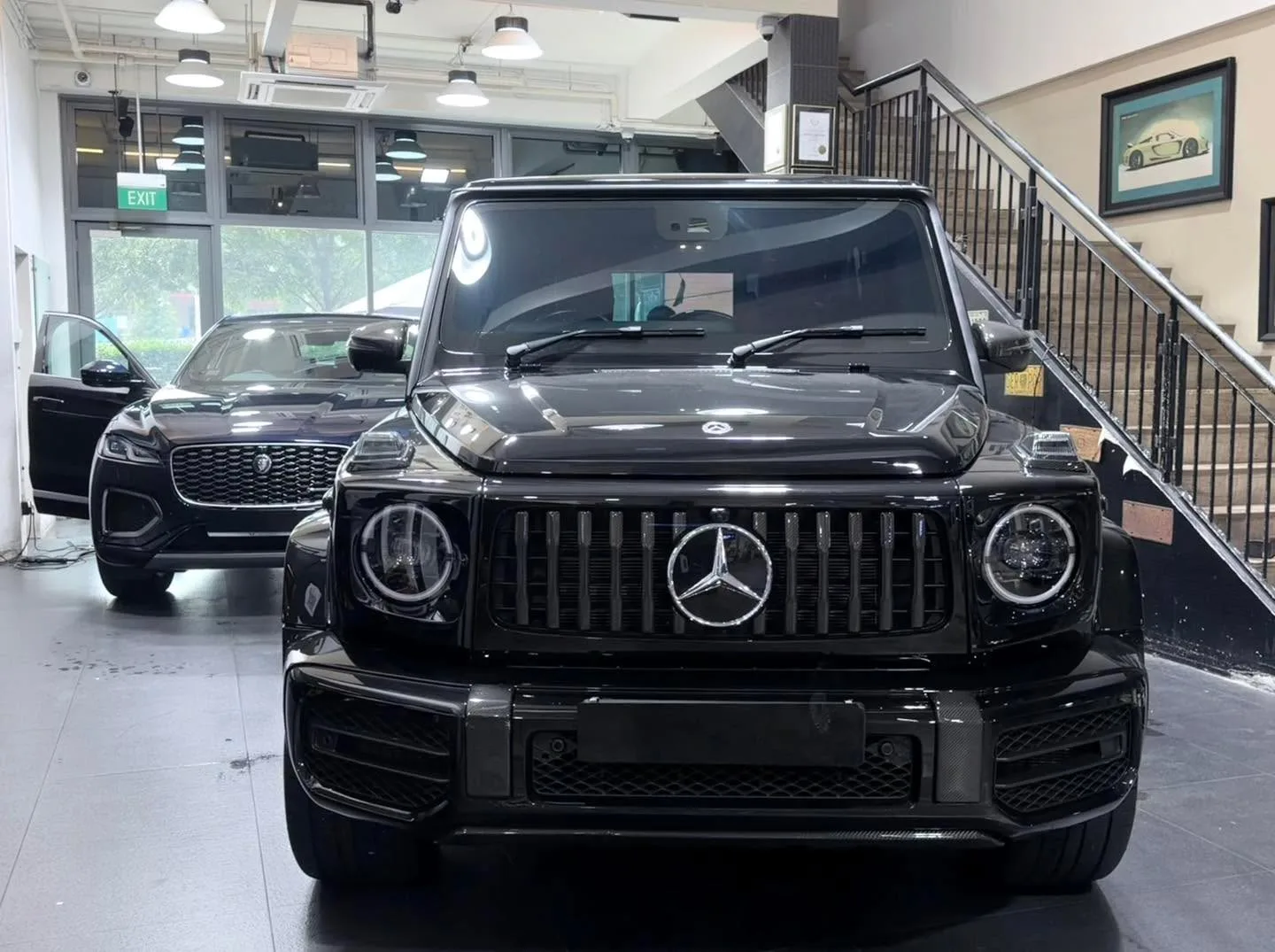 A black Mercedes-Benz G63 SUV viewed from the front in the workshop interior, with another black SUV visible in the background.
