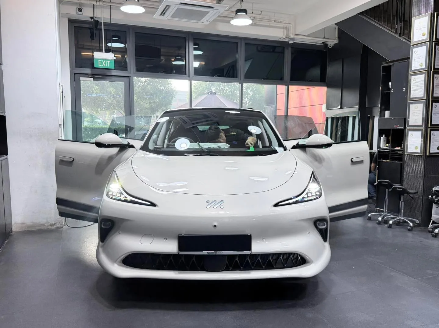 A white sports car with a door open, undergoing window tinting in the workshop.