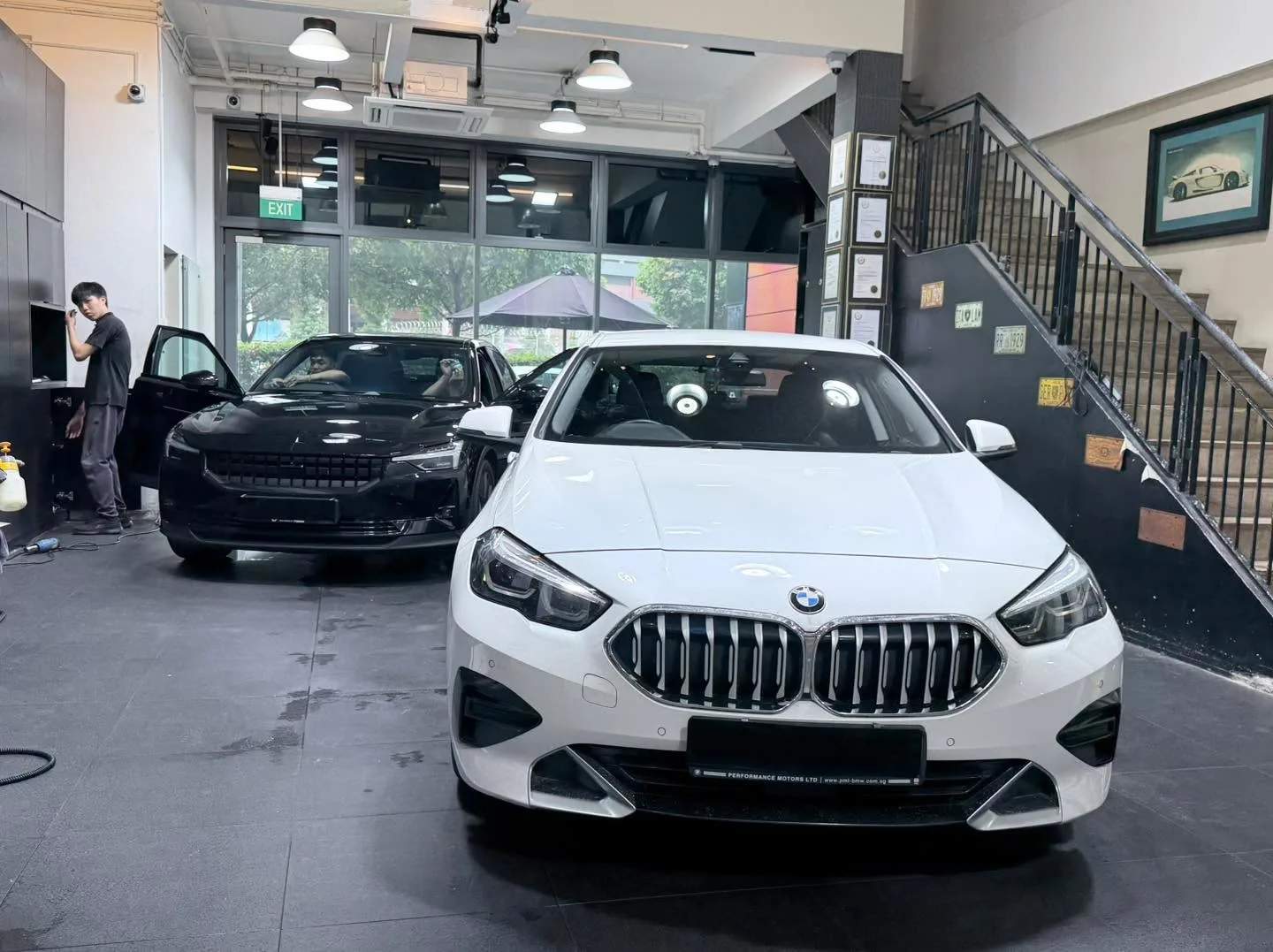A white BMW sedan and a black saloon with opened door, parked in the workshop interior.