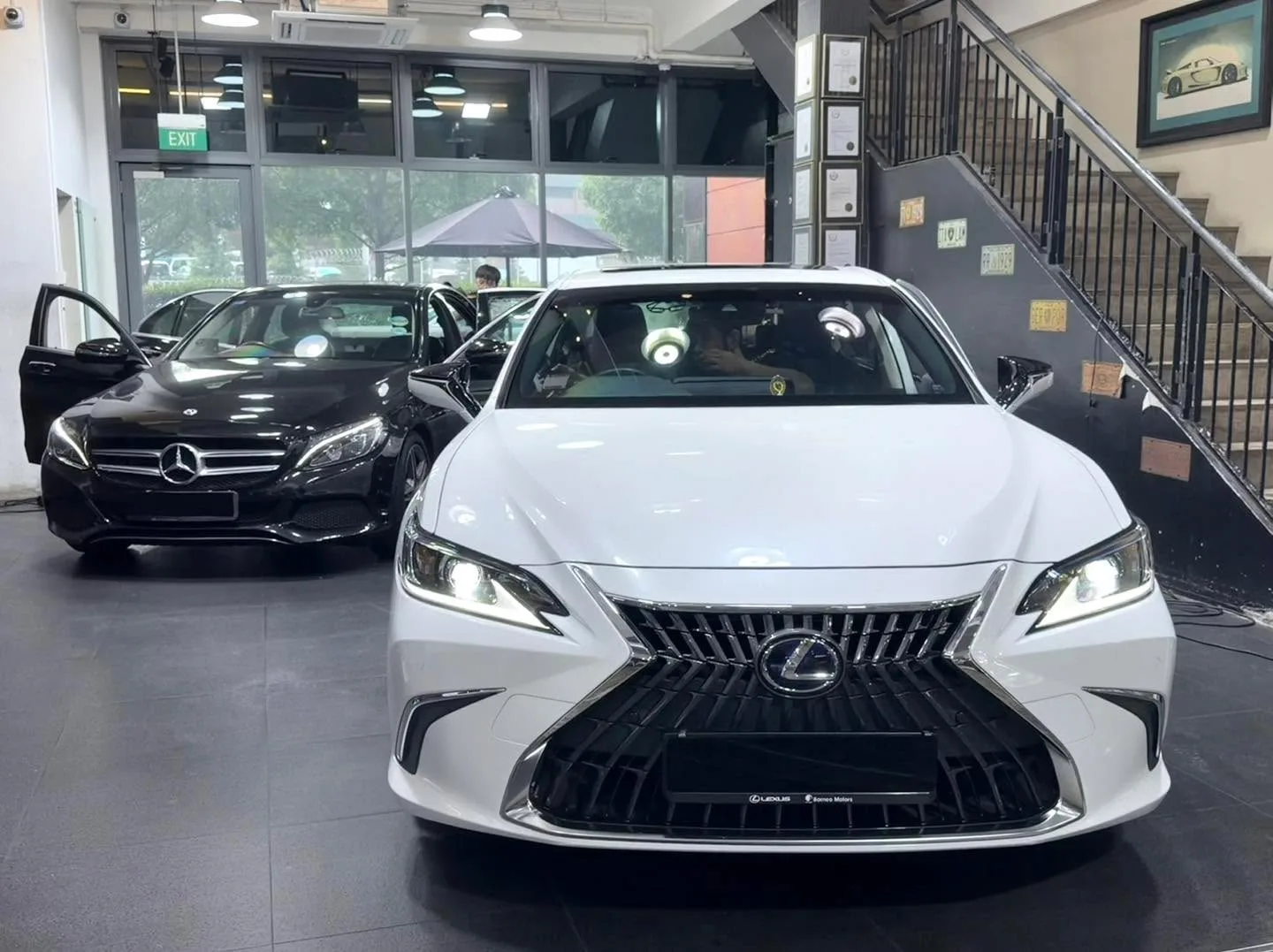 A white Lexus ES saloon in the foreground with a black car behind, both parked indoors.