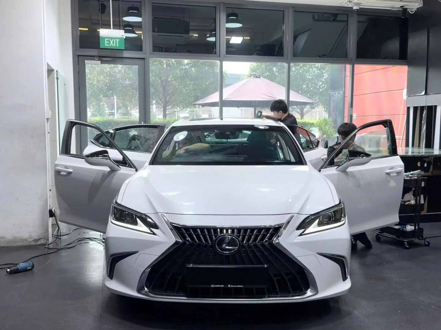 A white Lexus ES saloon with doors open, being prepared for window tinting by technicians.