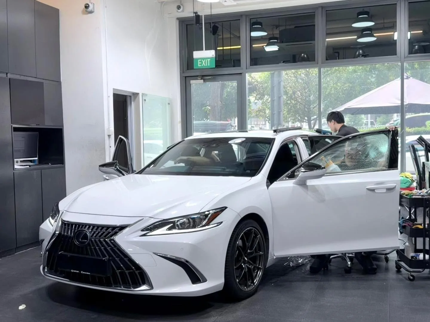 A white Lexus ES saloon with one door open, technician working on the window inside the workshop.