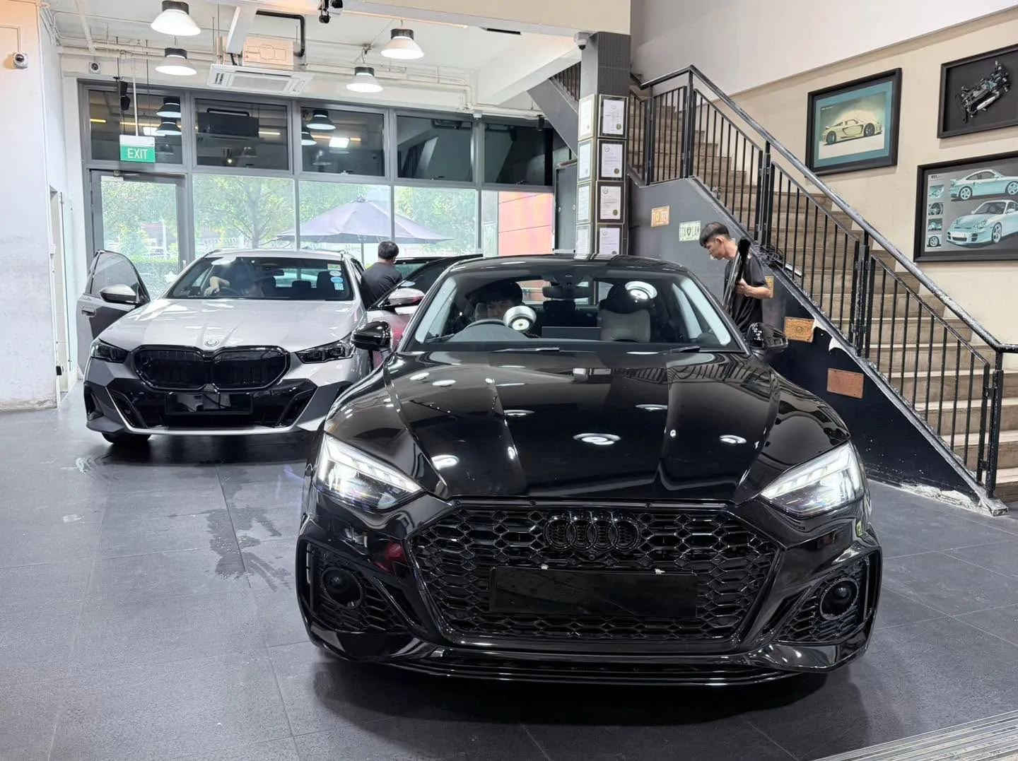 A black Audi A5 in the foreground and a white car behind it, both inside the workshop.