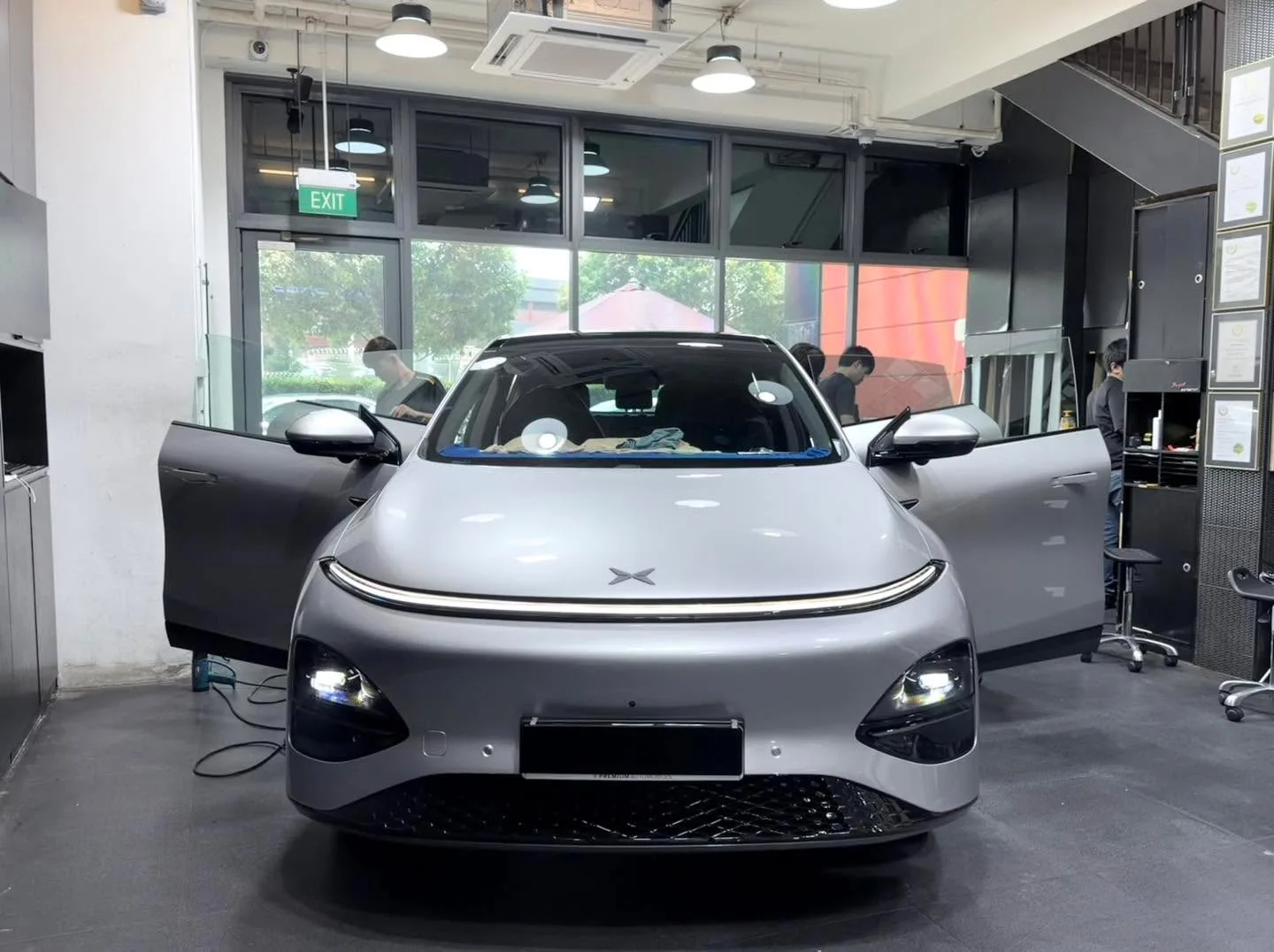 A silver XPENG G6 with doors open in the workshop bay, viewed from the front.