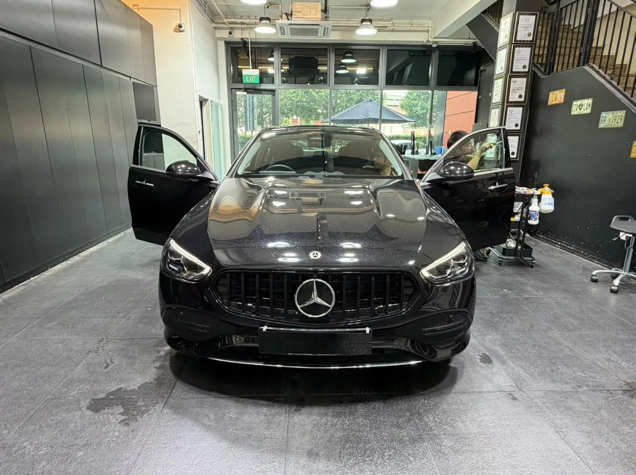 A black Mercedes-Benz C-Class photographed head-on in the workshop with doors open.