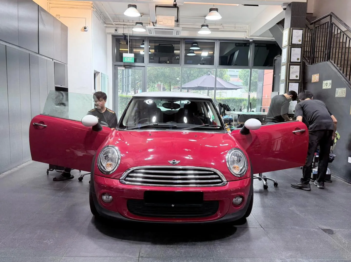 A red Mini Cooper R56 with open doors being worked on by staff in the workshop.
