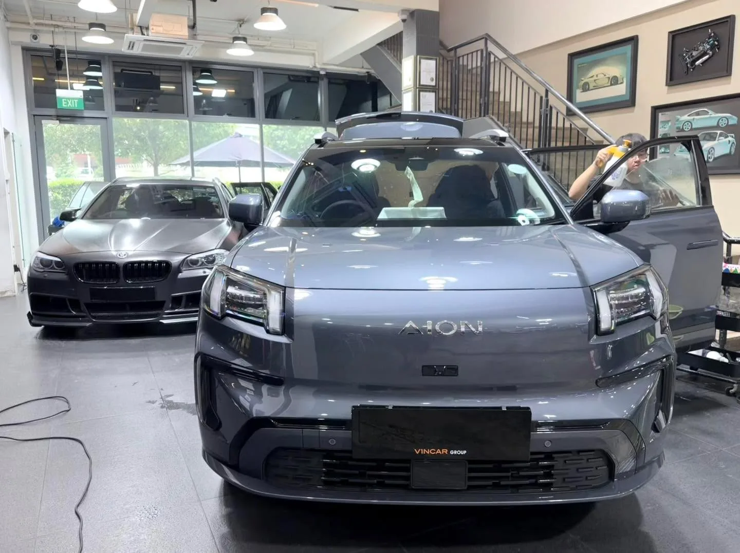 A grey GAC Aion SUV with distinctive badge, alongside a dark BMW saloon on the left.