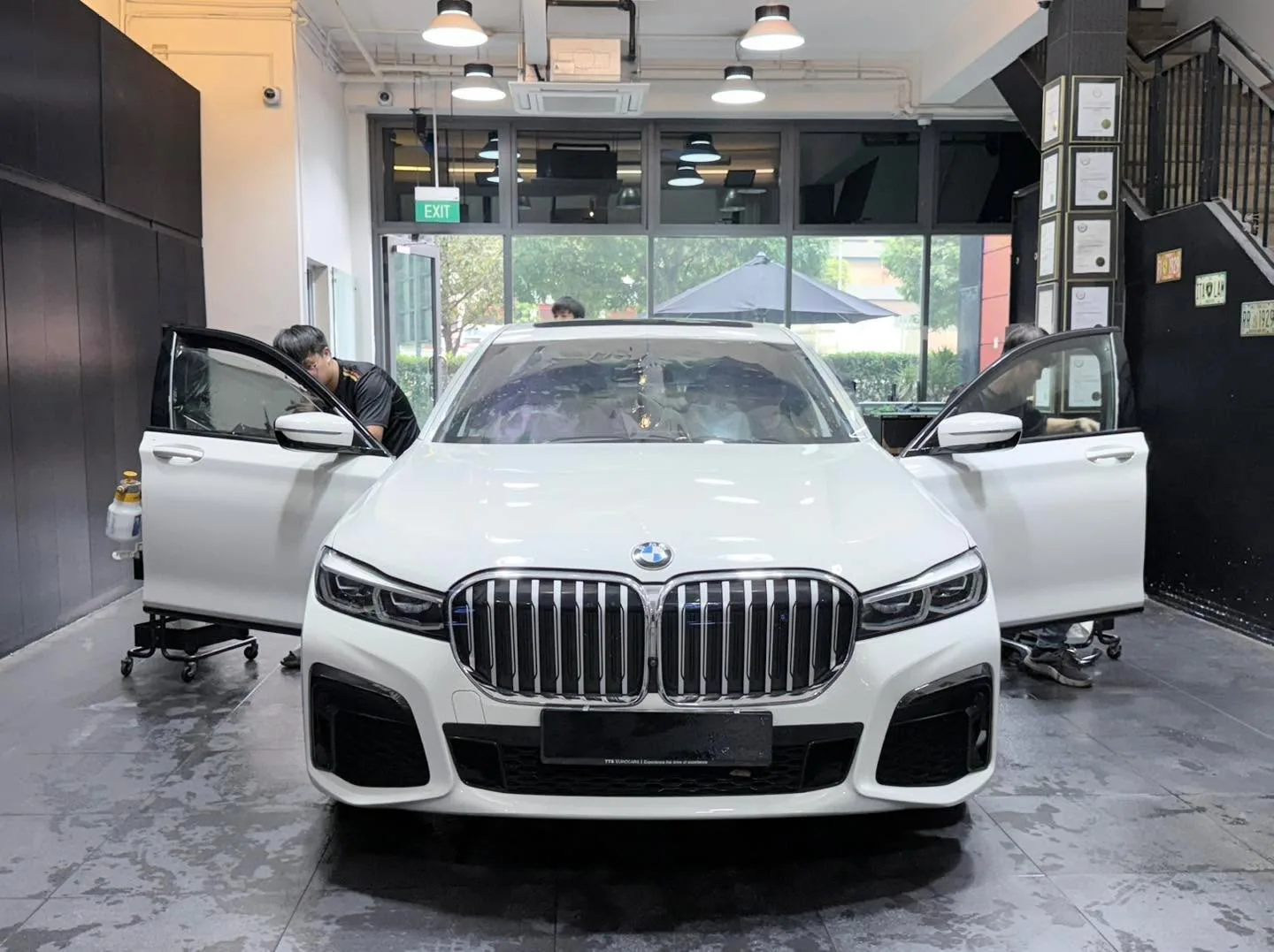 A white BMW 740 sedan facing forward with both doors open, technicians visible at the sides.